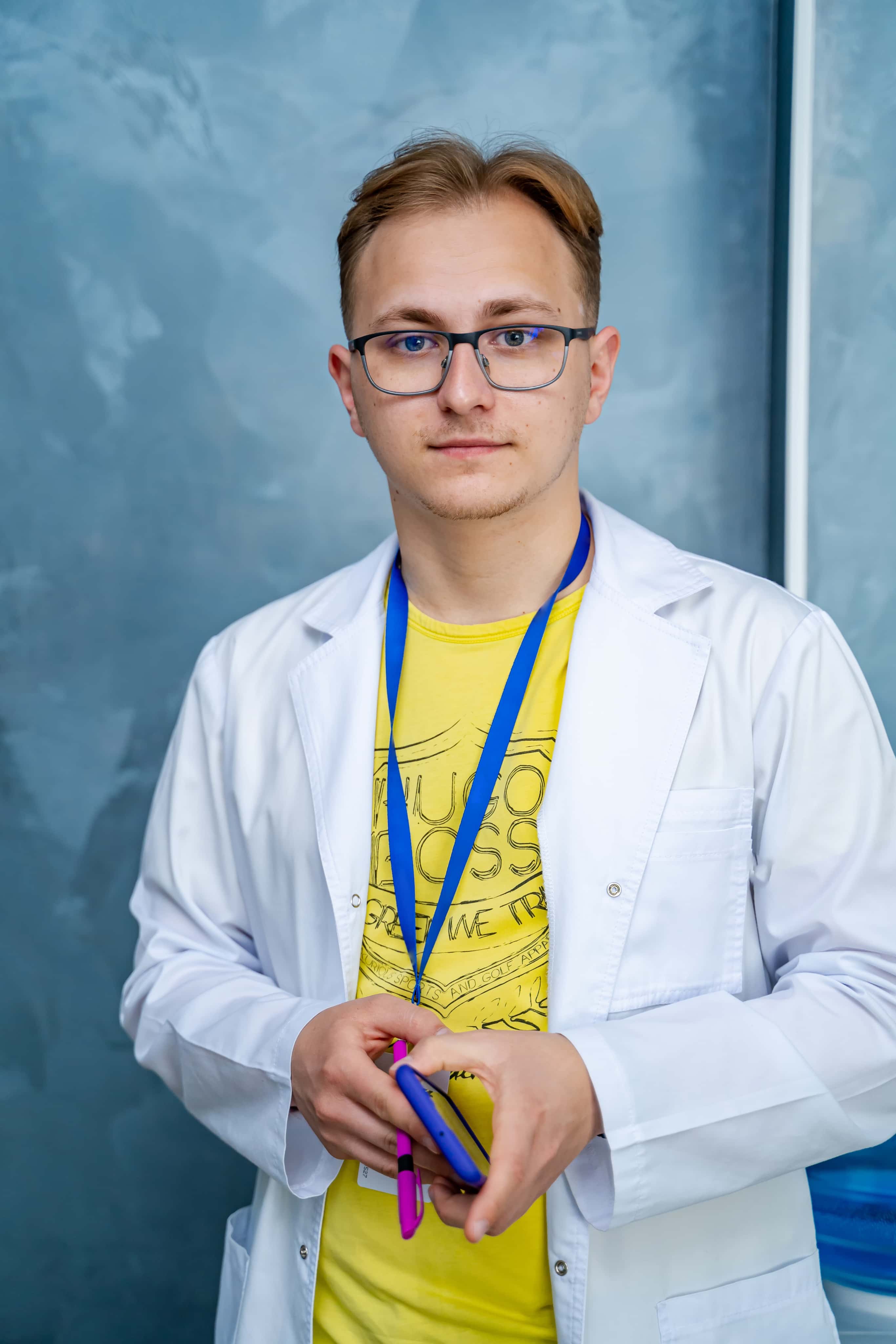 Nastolatek w białym fartuchu z identyfikatorem i telefonem w ręku, profil medyczny przygotowujący do zawodów lekarza i ratownika.