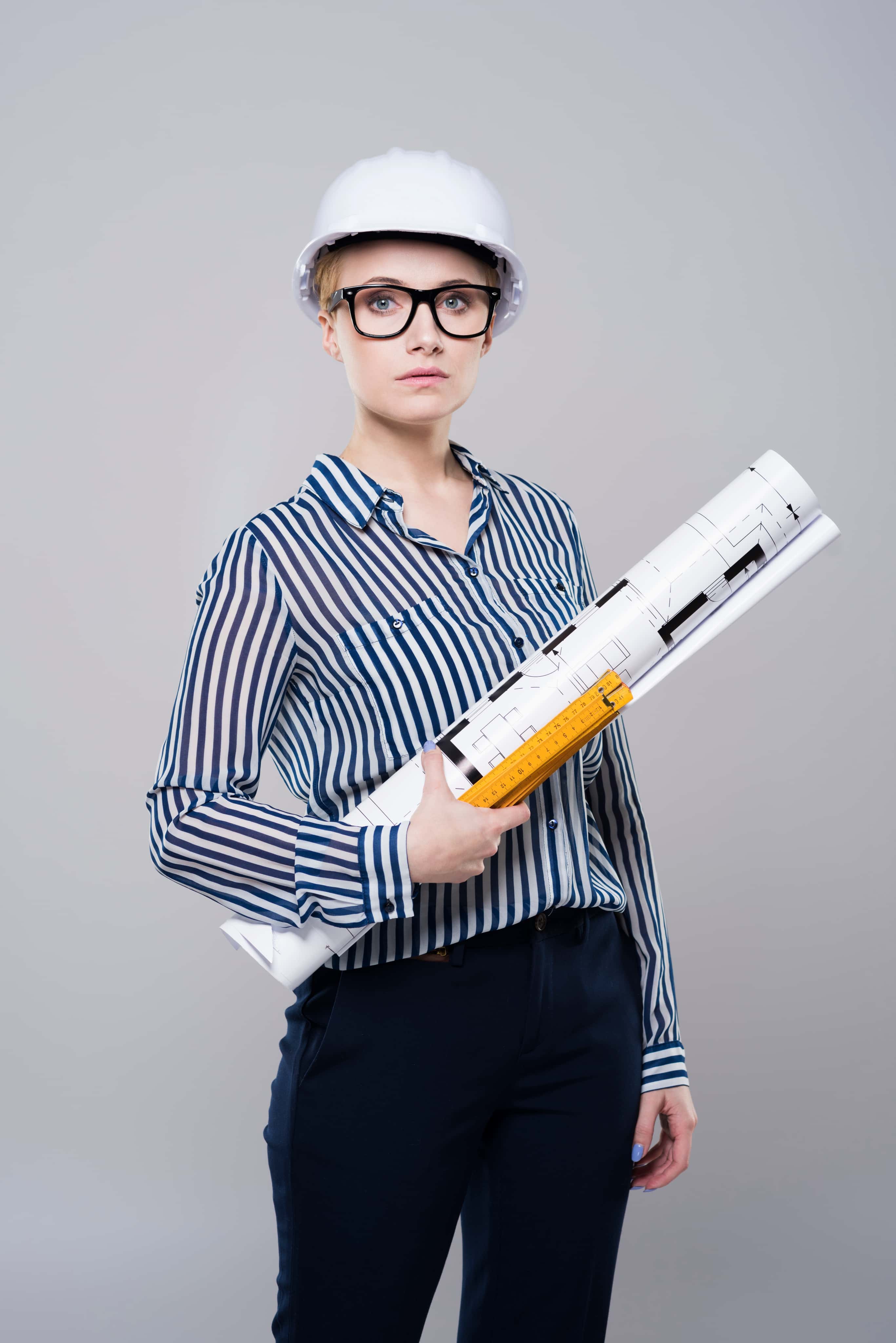 Dziewczyna w kasku ochronnym trzymająca zwinięte plany i linijkę, profil politechniczny z zainteresowaniem architekturą i inżynierią.