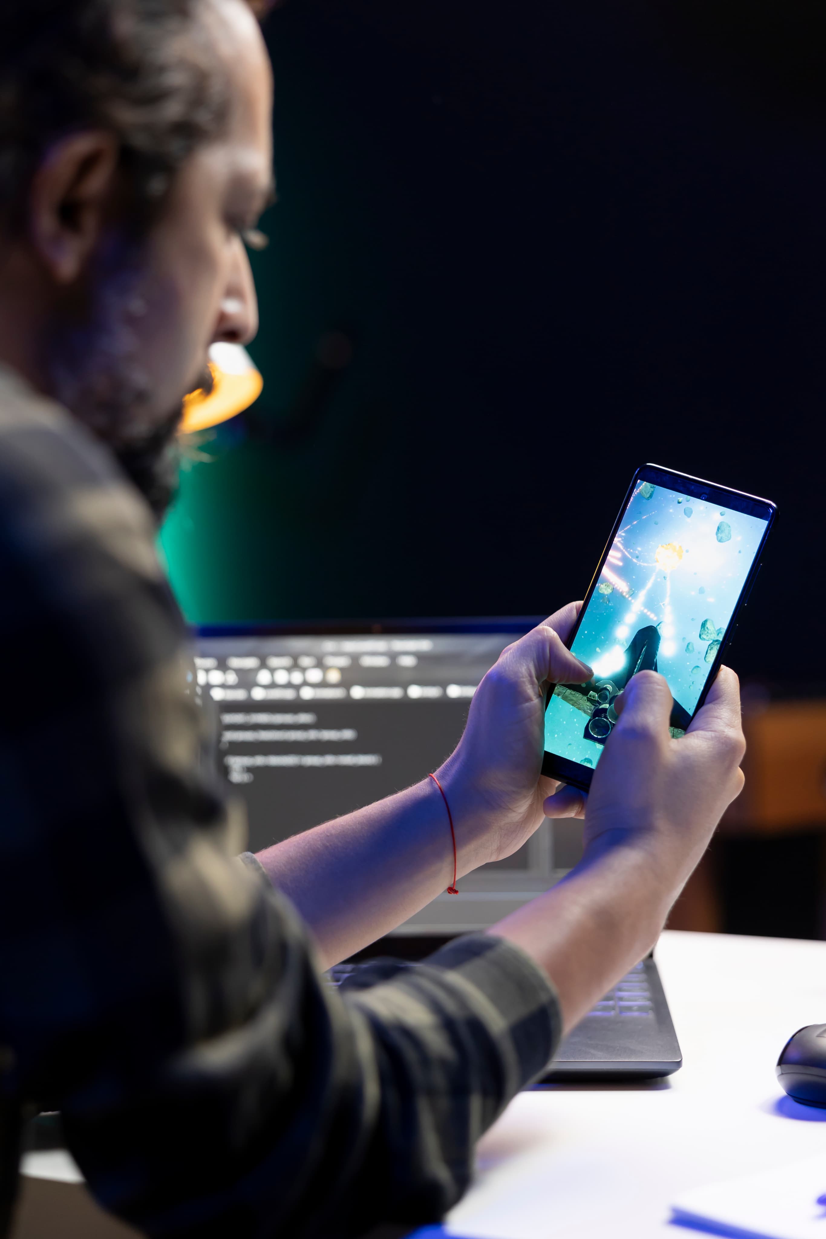 Programista testuje aplikację mobilną na smartfonie z kodem na laptopie w tle